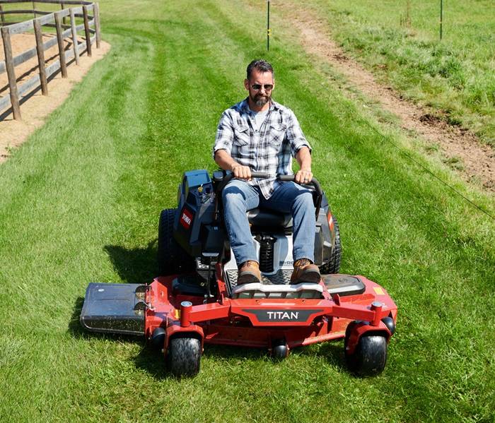 Person mowing green grass with a heavy-duty riding mower.