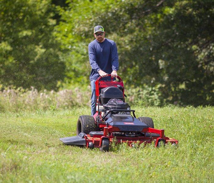 Person mowing green grass with a heavy-duty riding mower.